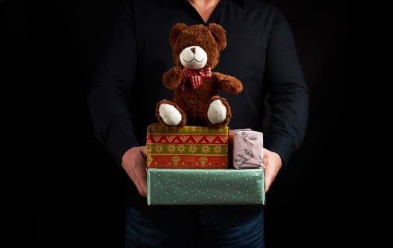adult man in a black shirt holds a blue square box tied with a red ribbon and brown teddy bear, concept of congratulations on Valentine's Day on February 14, low key 