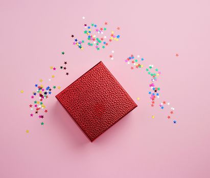 square red shiny box and multicolored sparkles on a pink background. Holiday concept. Package design. Festive concept.