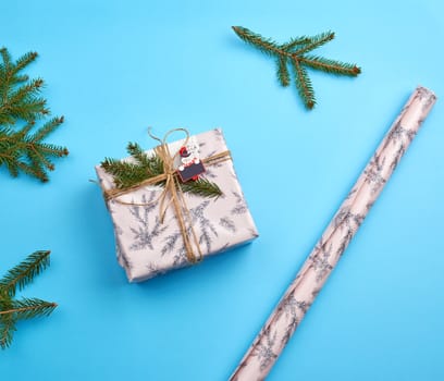 gift wrapped in pink paper and tied with a brown rope, decor from a green spruce branch on a blue background, top view