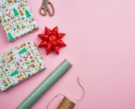 rolls with wrapping paper, brown rope, scissors, decor and a wrapped square box with a gift. DIY gift making process, pink background