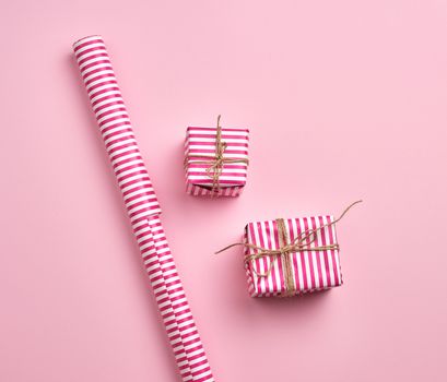 two gifts wrapped in pink striped paper and paper roll on a pink background, top view, copy space
