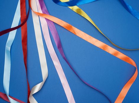 many silk multi-colored ribbons on a blue background, top view