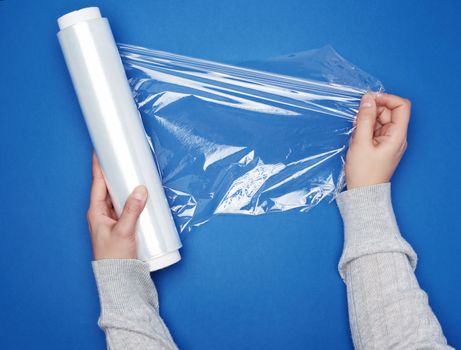 hand hold a large roll of wound white transparent film for wrapping food, top view, blue background 
