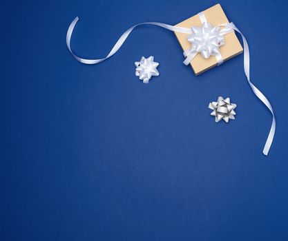 brown square box with a gift tied with a white ribbon with a bow on a blue classic background, top view, empty place for an inscription