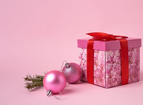 pink gift box with bow, green spruce branch and two decorative pink balls on a pink background