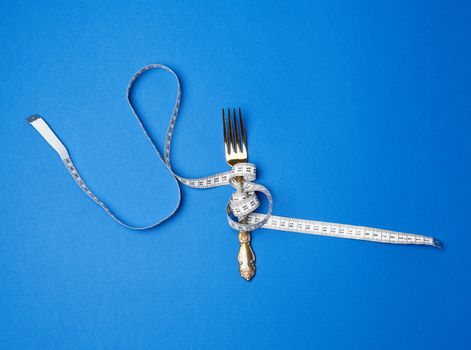 iron fork  wrapped in a measuring tape on a blue background, top view