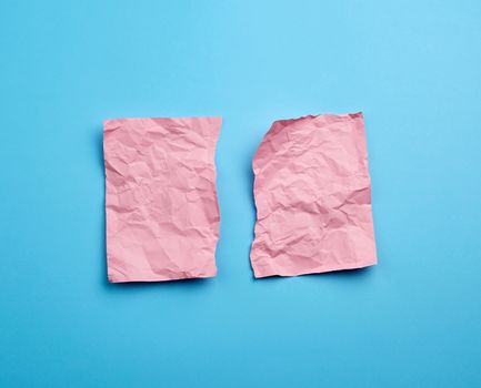 crumpled pink sheet of paper torn in two on a blue background. Paper piece torn edge.