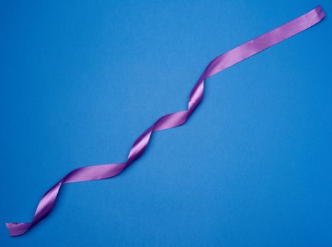 purple silk thin ribbon twisted on a blue background, trendy color, top view