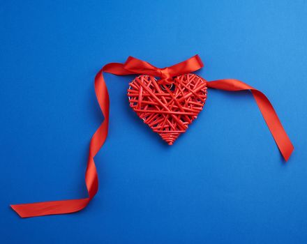 red wicker decorative heart hanging on silk ribbon, blue festive background for Valentine's day