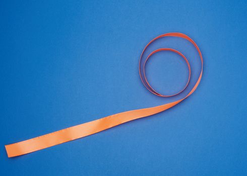 orange silk thin ribbon twisted on a blue background, trendy blue color, top view