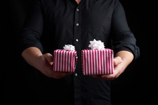 adult man in a black shirt holds in his hand a stack of paper-wrapped gifts, concept of holiday greetings, low key