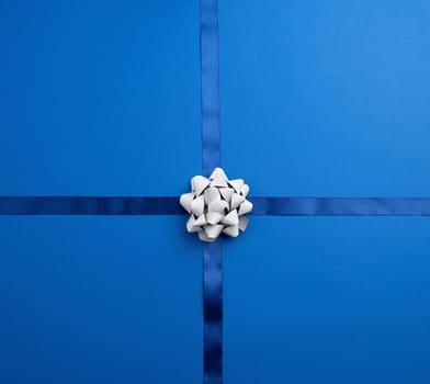 blue silk ribbon crossed on a dark blue background, in the middle a silver bow, imitation of tying a gift, top view