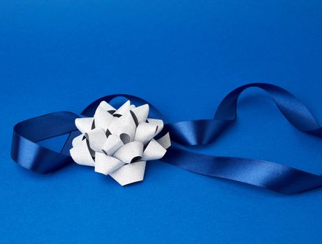blue silk thin ribbon twisted and gray shiny bow on a blue background, trendy classic color, close up