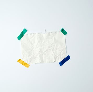 white crumpled sheet of paper torn from a spiral notebook and glued with multi-colored electrical tape on a white background, place for text