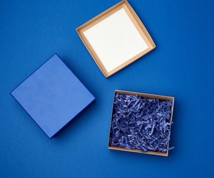 open brown square cardboard empty box, item lies on a blue classic background color, top view