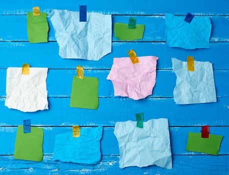 many torn multicolored pieces of paper glued with scotch tape on a blue wooden background, place for text