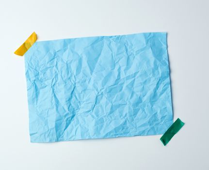 blue crumpled sheet of paper glued with adhesive tape on a white background, place for text