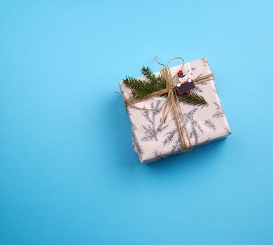 gift wrapped in pink paper and tied with a brown rope, decor from a green spruce branch on a blue background, top view