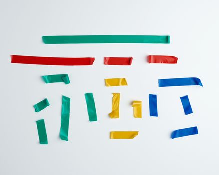 set of torn multicolored rubber pieces of electrical tape glued to a white background, close up