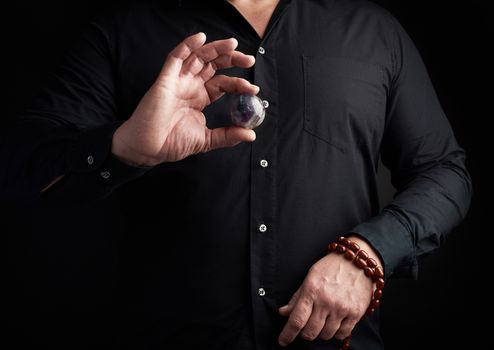 man in a black shirt holds a stone ball for religious rituals, meditations, dark background