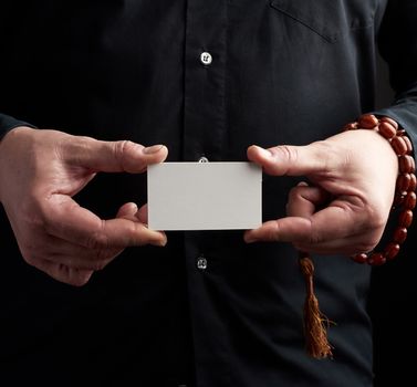 two male hands holding a rectangular blank white paper business card, a man wearing a black shirt, place for inscription