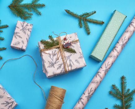 gift wrapped in pink paper and tied with a brown rope, decor from a green spruce branch on a blue background, top view
