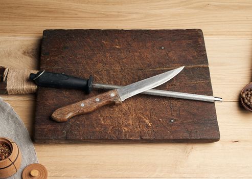 old sharp knife and sharpener with a handle on a wooden background, top view