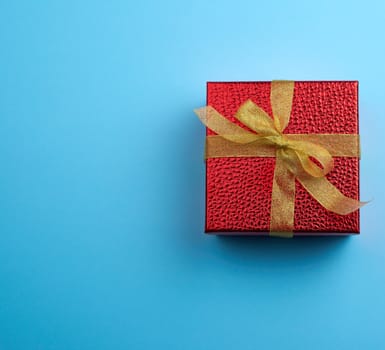 square red box tied with a golden ribbon, concept of congratulations and gifts, top view, blue background