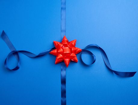 blue silk ribbon crossed on a dark blue background in the middle of a red bow, imitation of tying a gift, top view