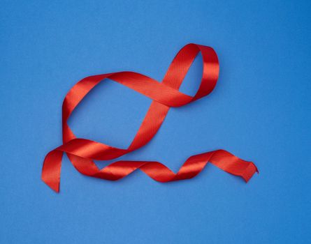 red silk thin ribbon twisted on a blue background, trendy color, top view