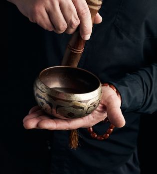 man in a black shirt rotates a wooden stick around a copper Tibetan bowl. ritual of meditation, prayers and immersion in a trance. Alternative treatment