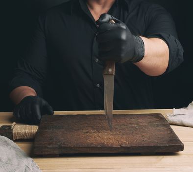 chef in a black shirt and black latex gloves holds a large kitchen knife for cutting meat, low key