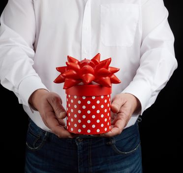 adult man in a white shirt holds a round gift cardboard box with a bow, concept of a congratulation on the holiday, anniversary, surprise