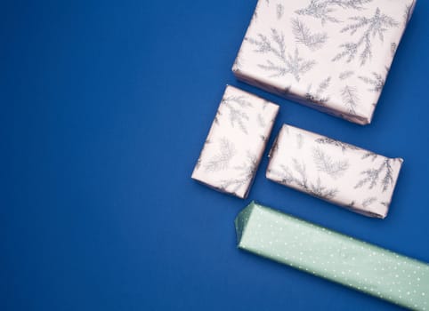 gifts wrapped in colored paper on a blue background, top view, copy space