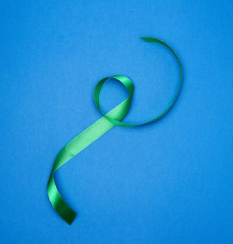 green silk thin ribbon twisted on a blue background, top view