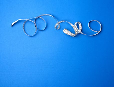 twisted measuring tape on a blue background, copy space
