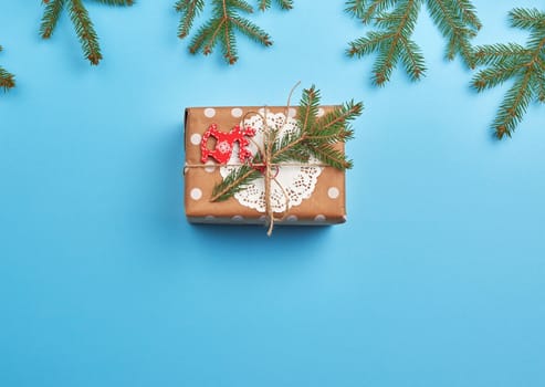 gift wrapped in brown craft paper and tied with a brown rope, decor from a green spruce branch on a blue background, top view
