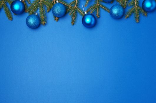 green spruce branches, blue shiny Christmas balls on a blue background, festive backdrop for Christmas and New Year, place for an inscription