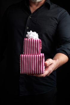 adult man in a black shirt holds in his hand a stack of paper-wrapped gifts, concept of holiday greetings, low key
