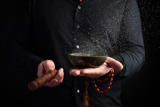 adult man in a black shirt rotates a wooden stick around a copper Tibetan bowl with water. ritual of meditation, prayers and immersion in a trance. Alternative treatment