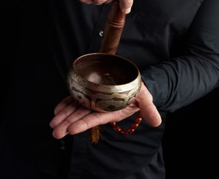 man in a black shirt rotates a wooden stick around a copper Tibetan bowl. ritual of meditation, prayers and immersion in a trance. Alternative treatment