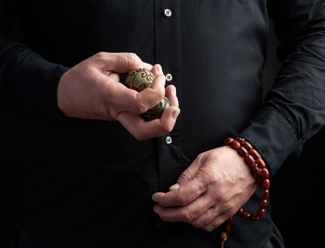 man in a black shirt holds a green stone ball for religious rituals, meditations, dark background