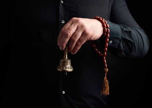 adult man in a black shirt holds a copper Tibetan ritual bell, low key. bell represents the feminine principle of excellence in wisdom.
