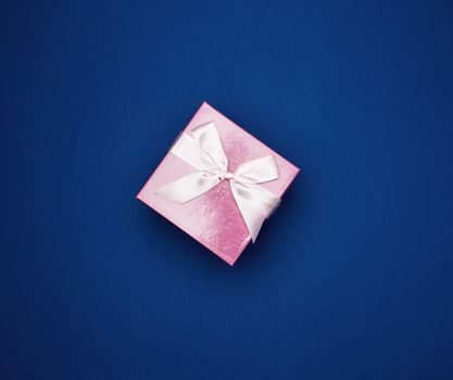 square closed pink box with white bow on a blue background, top view, empty place for an inscription
