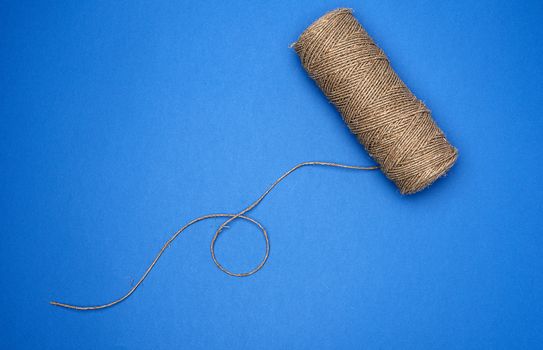 whole coil of twisted brown rope jute tourniquet, eco-friendly packagingm blue background 