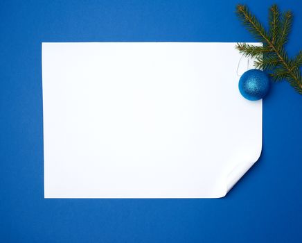 white blank sheet of paper with a curled bottom corner and a green sprig of spruce, background for a greeting lettering for Christmas