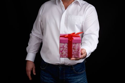 adult man in a white shirt holds a pink gift cardboard box with a bow, concept of a congratulation on the holiday, anniversary, surprise