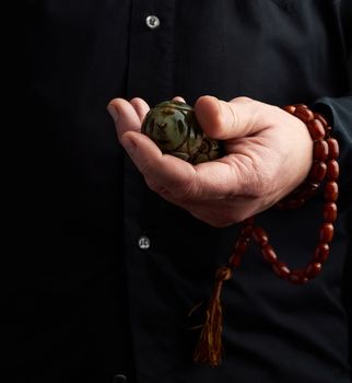 man in a black shirt holds a green stone ball for religious rituals, meditations, dark background