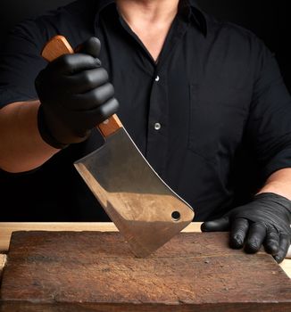 chef in a black shirt and black latex gloves holds a large kitchen knife for cutting meat, low key