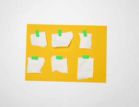 set of variously shaped empty pieces of white paper glued with green velcro on a yellow sheet of paper, white background, close up